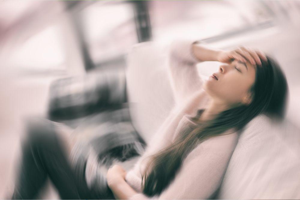 A woman feels dizzy while sitting on a sofa.