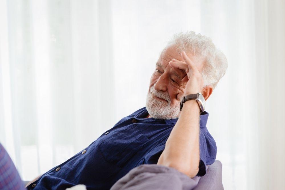 Vaskulaarista dementiaa sairastava mies istuu surullisena sohvalla.